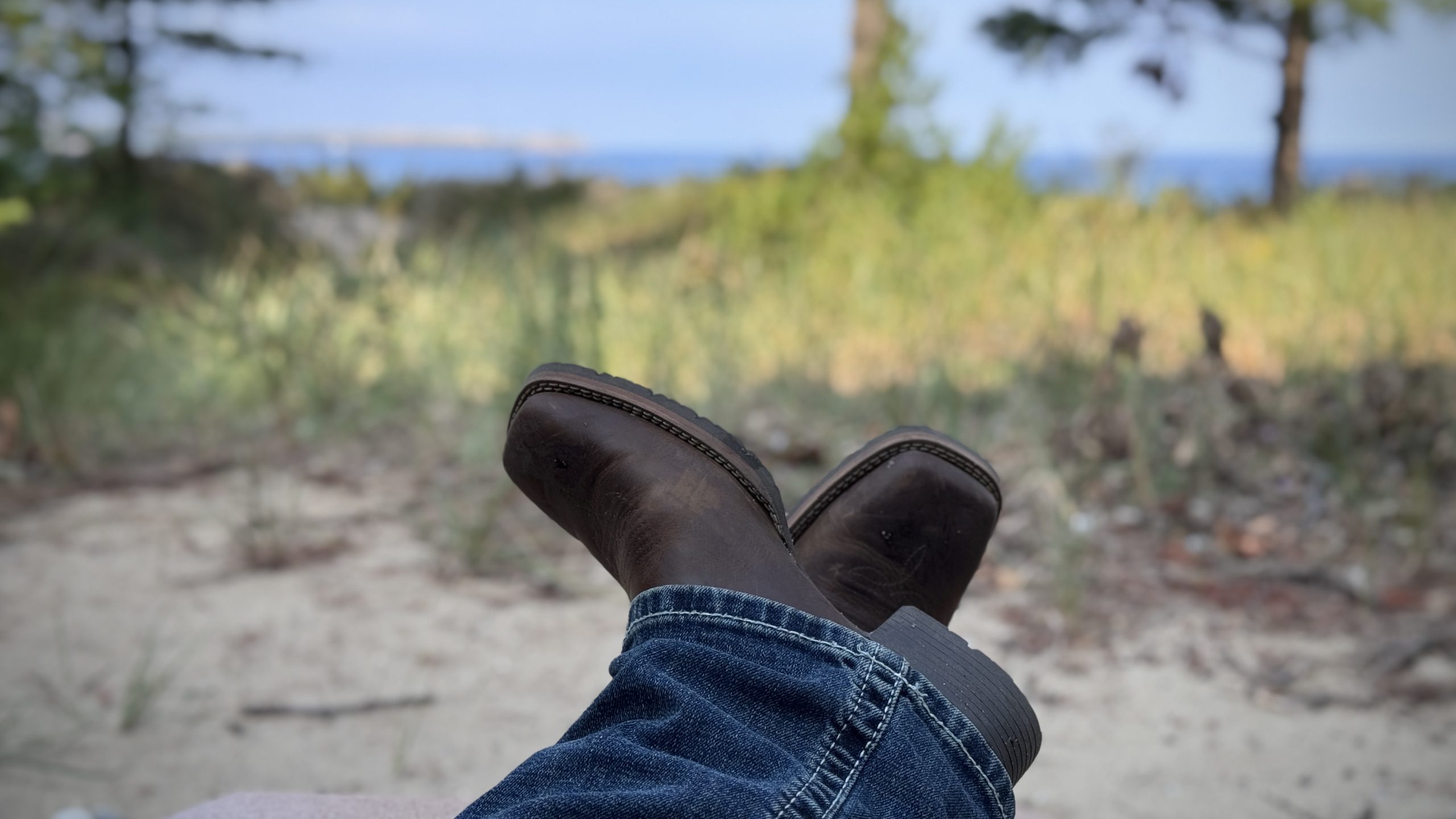 Crossed boots resting on a sandy dune with beach grass in the background