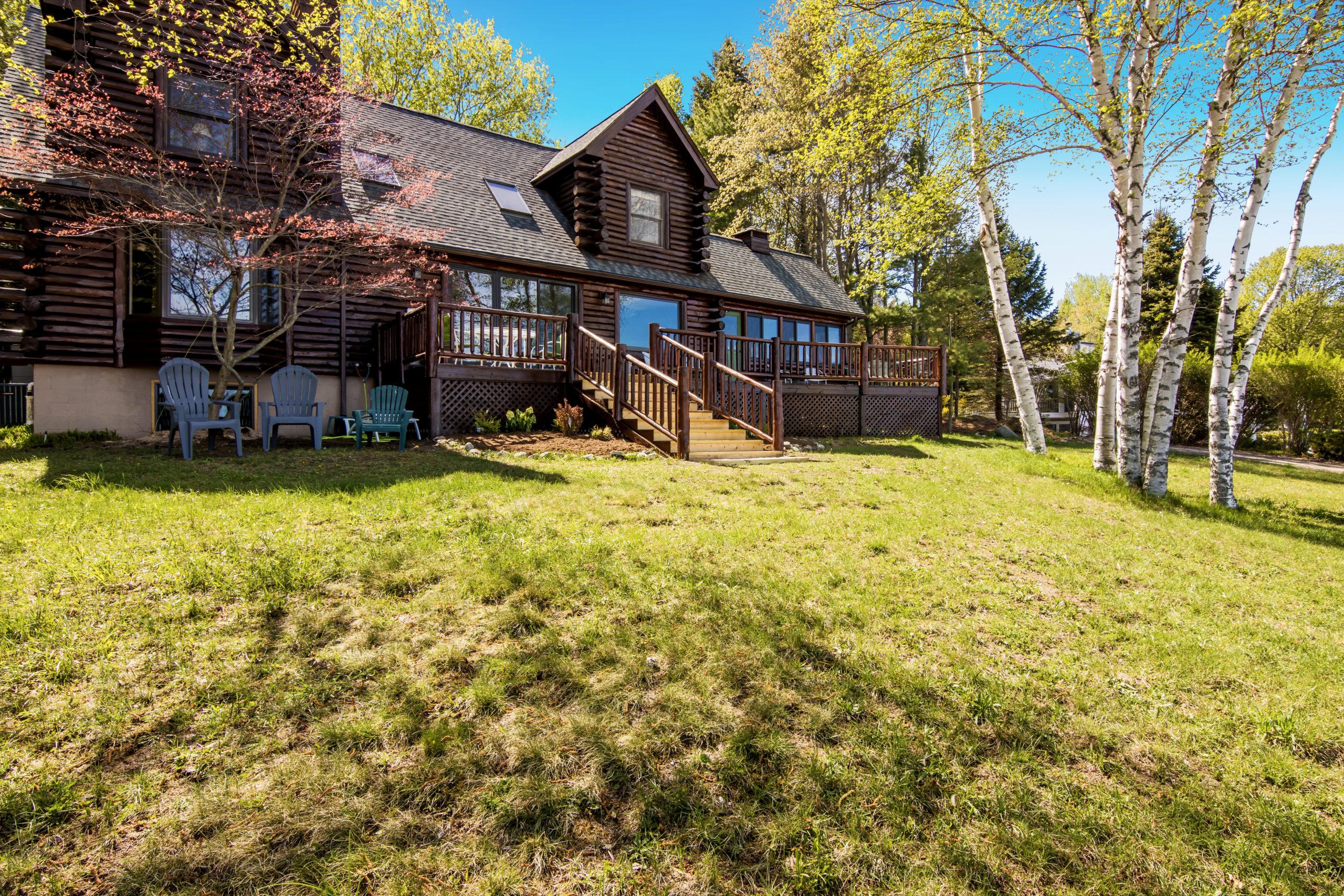 Log lodge with a deck seen across a lawn with birch trees