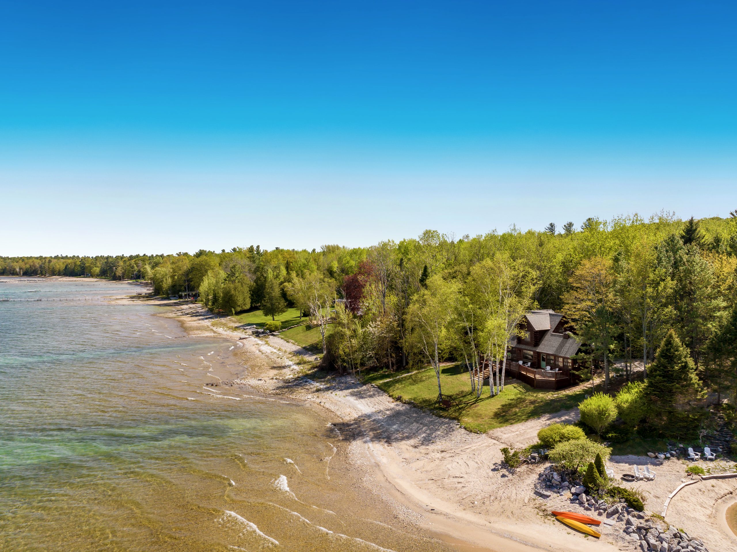 Aerial view of a rocky shoreline with turquoise water and woods near M22 Lakefront Lincoln Lodge in Northport