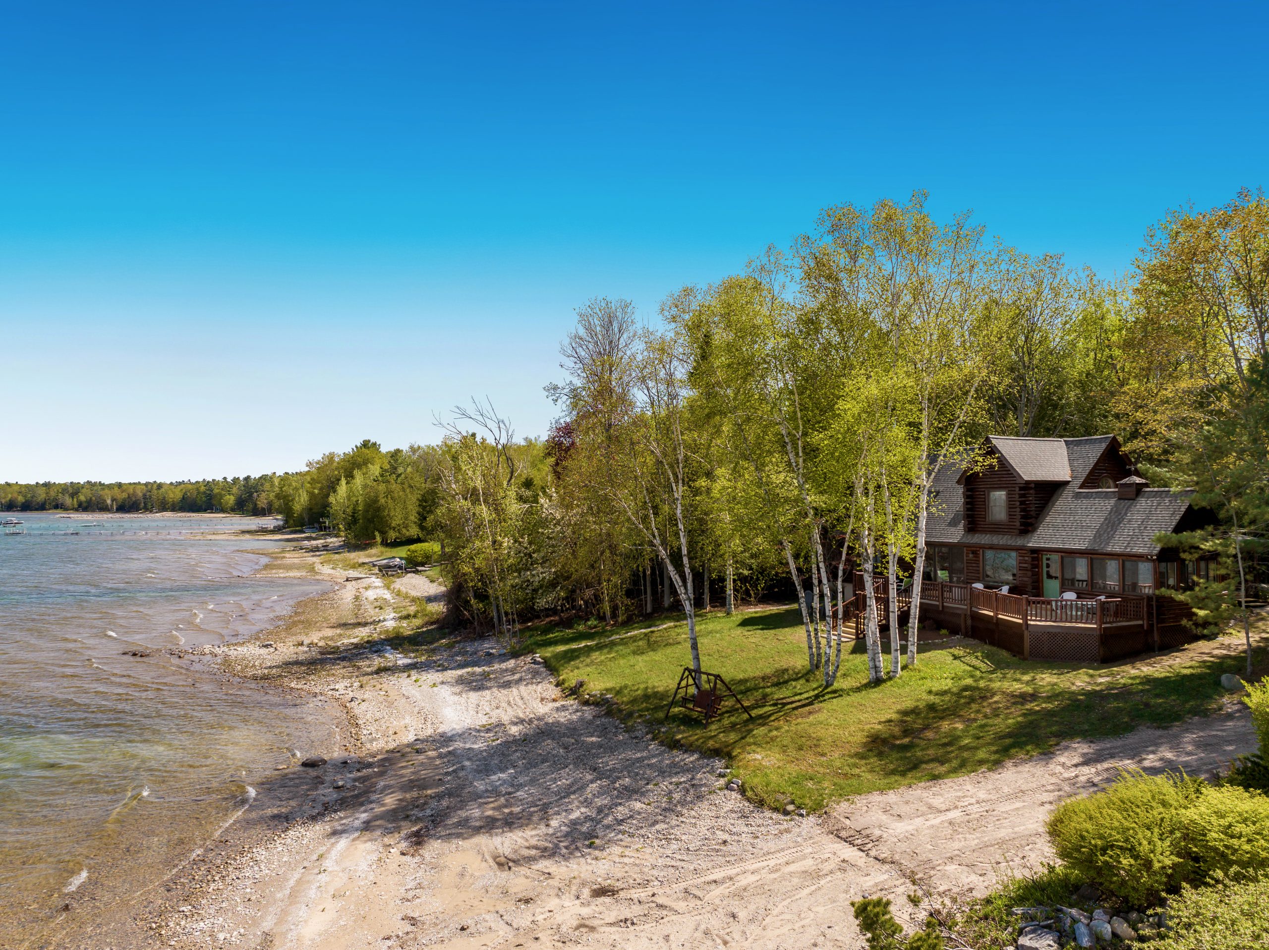 Aerial view of the lodge among birch trees above a pebbly beach at M22 Lakefront Lincoln Lodge in Northport, Michigan