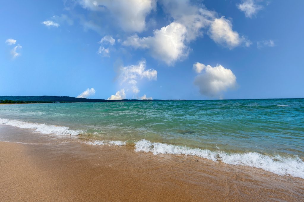 Turquoise Lake Michigan surf on a sandy shore beneath blue sky and white clouds near Glen Arbor, Michigan