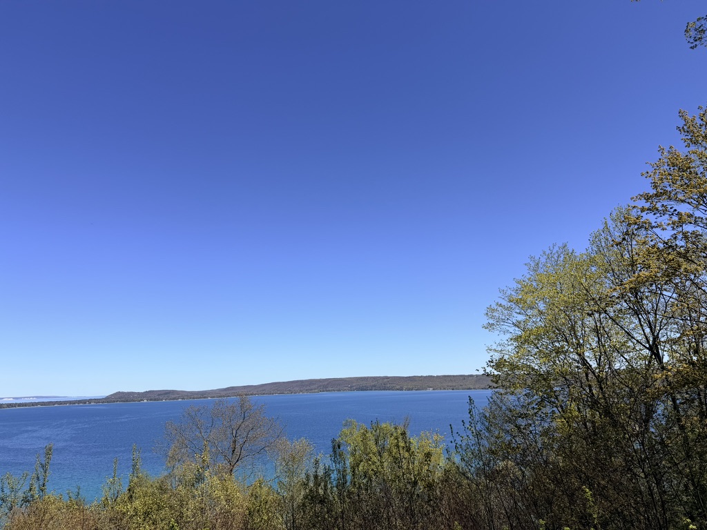 Wide blue lake seen from a wooded rise through green and autumn-tinged trees