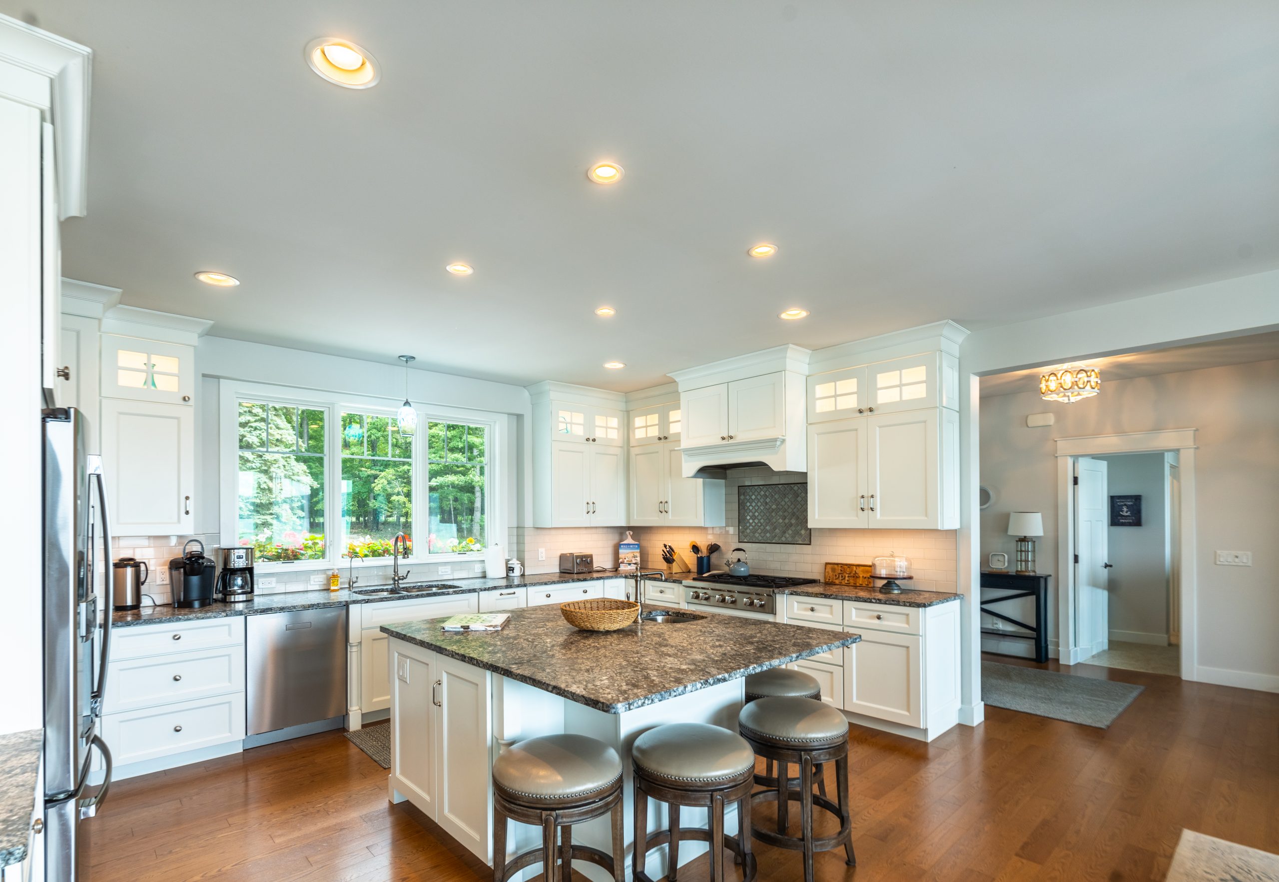 White kitchen with a granite island, bar stools and stainless appliances at Glen Den in Empire, Michigan
